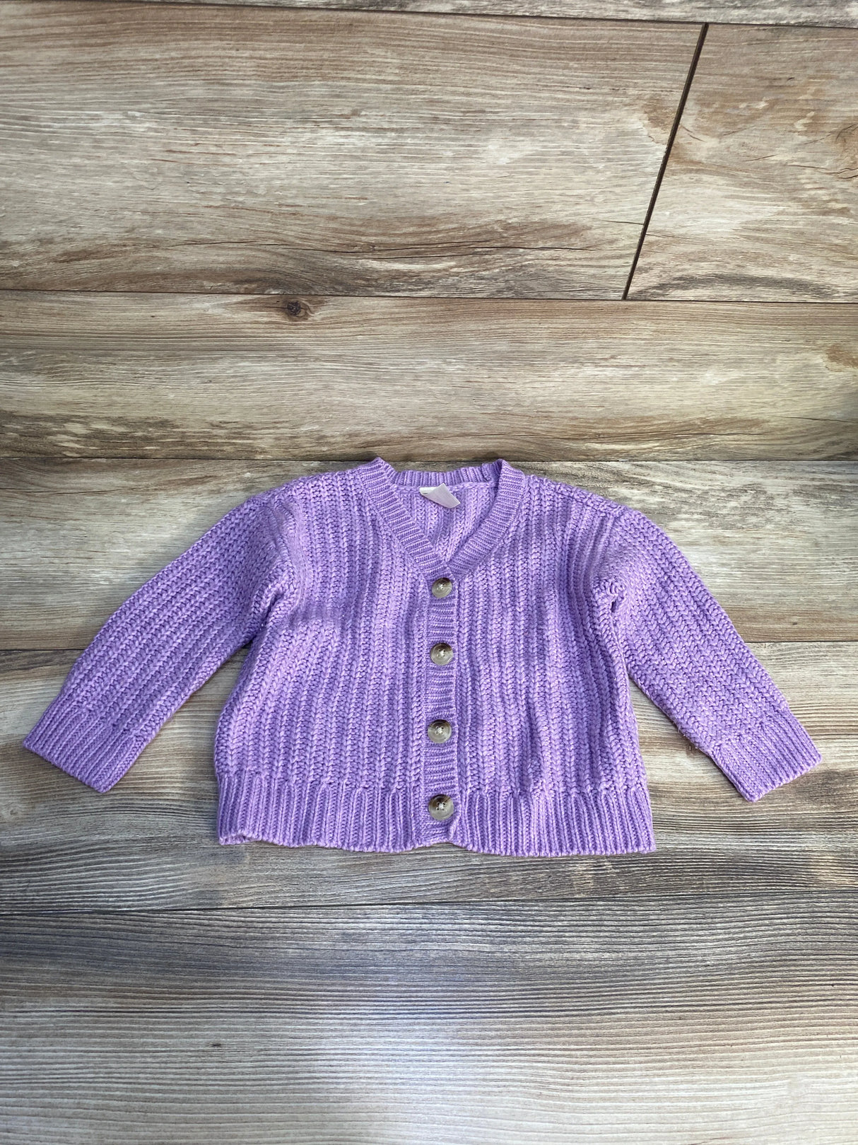 Purple knit baby cardigan with buttons on wood background