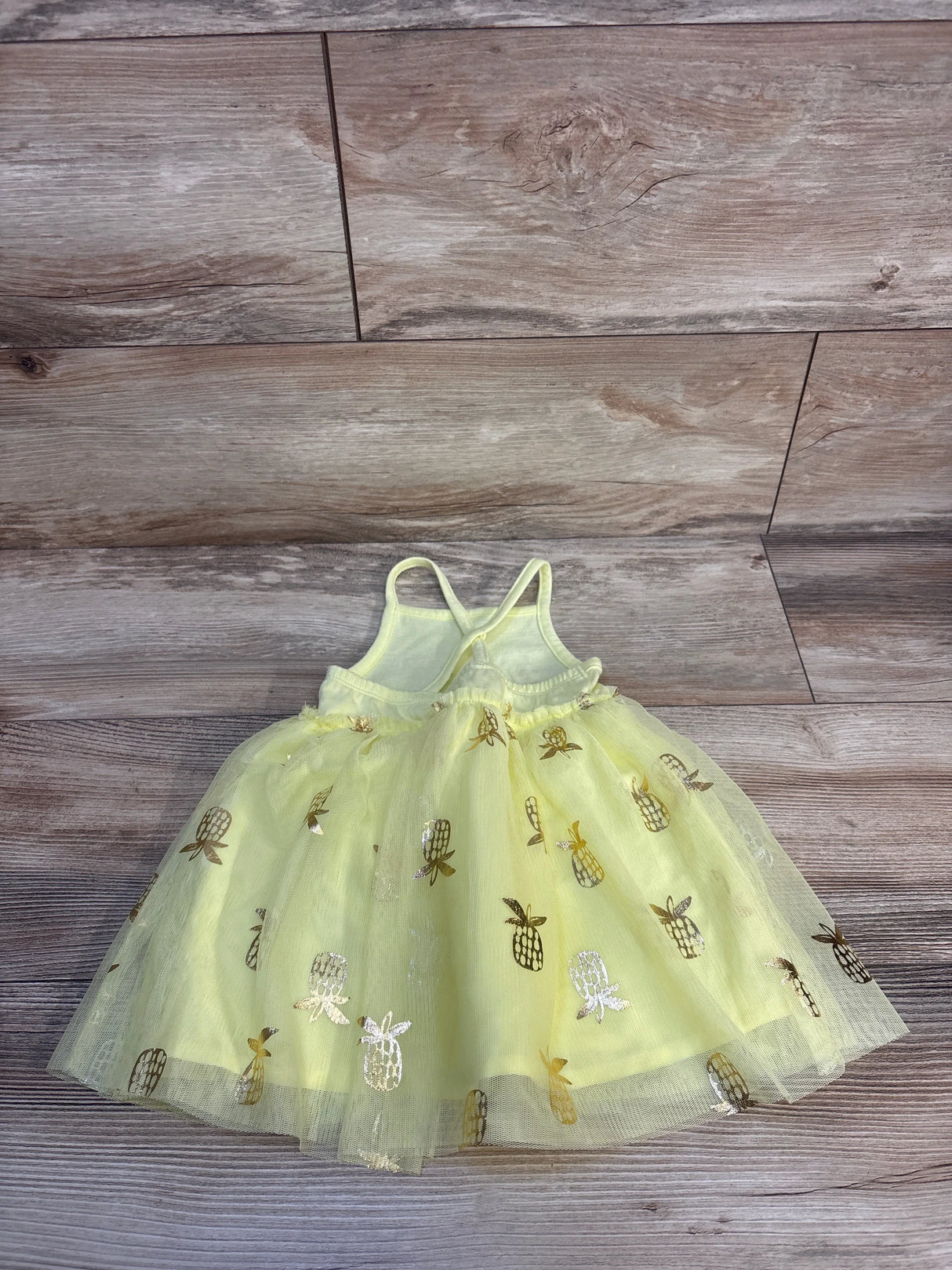 Flat lay of Cat & Jack yellow tulle tank dress with gold pineapple foil print and layered tulle skirt on wood background