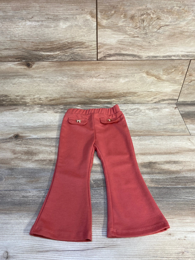 Flat lay of red flared toddler pants (18m) showing elastic waistband and back pockets with gold bow charms on wood background