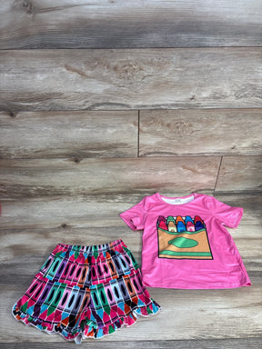 Flat lay of pink toddler crayon t-shirt with crayon box graphic and matching multicolor crayon-print ruffle shorts on wood plank background