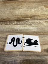 Front view of Lovevery wooden board book open to black snake and mouse illustrations on white pages on a wood tabletop