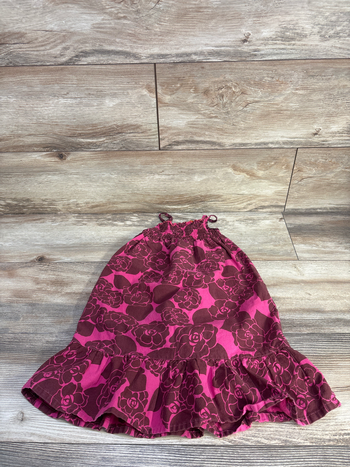 Flat lay of girls' RubiMoon floral smocked dress showing smocked top with tie straps and ruffled hem on wood floor