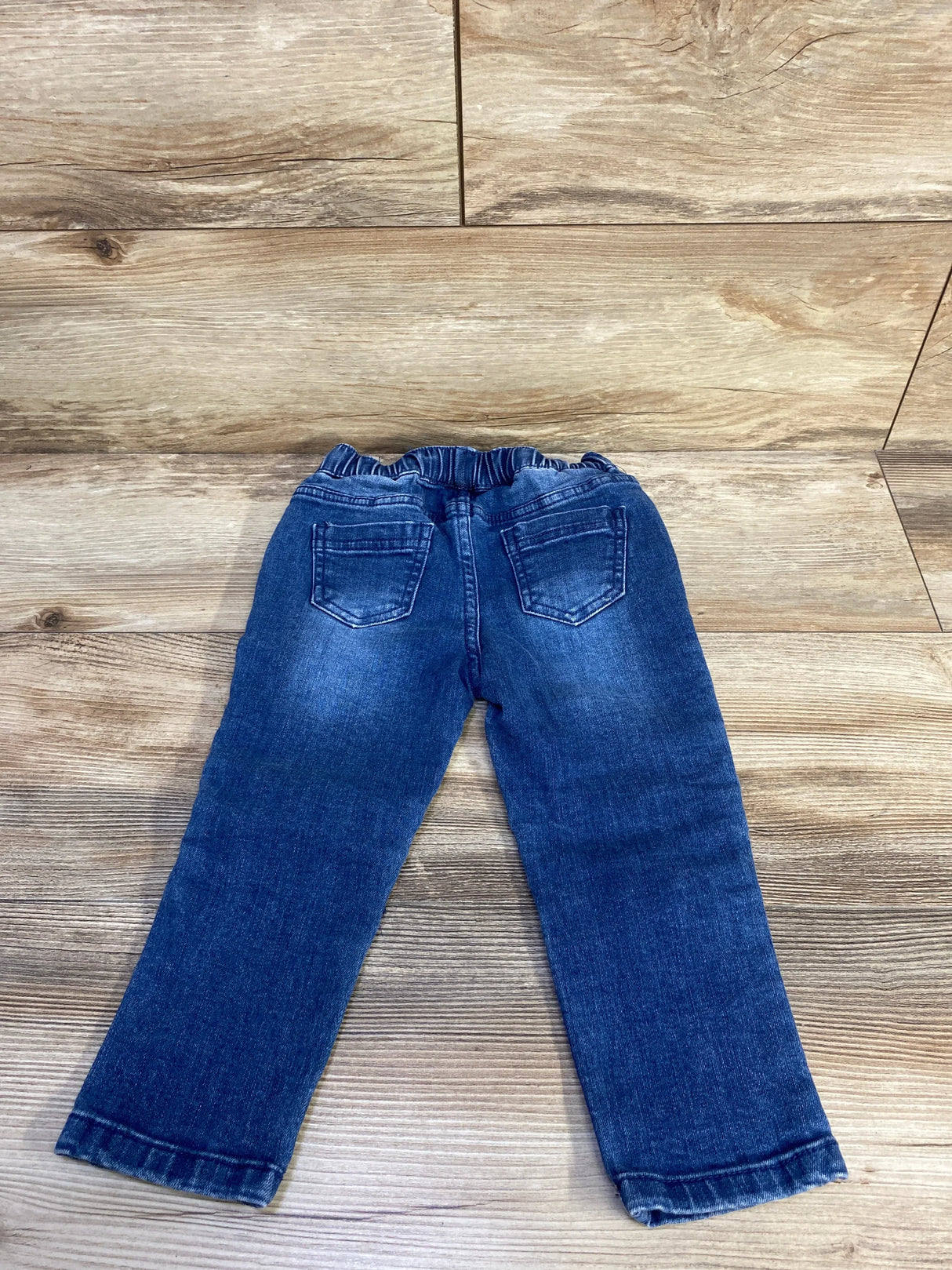 Back view of toddler blue Art Class drawstring jeans showing elastic drawstring waist and back pockets on wood background