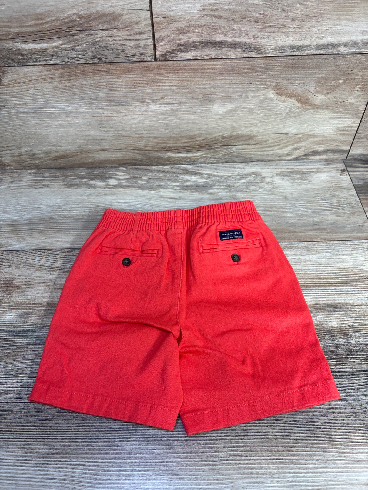 Back view of red Janie and Jack toddler twill shorts, elastic waist and buttoned back pockets on wood background