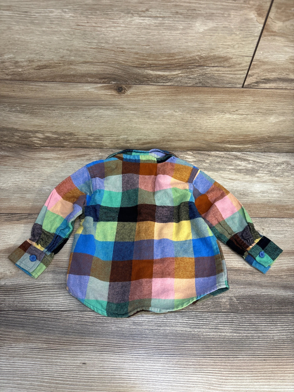 Colorful plaid flannel long sleeve toddler shirt laid flat on wood floor