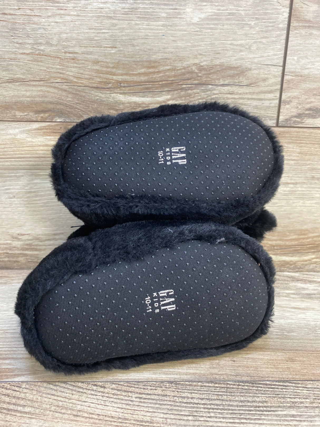 Black faux fur baby slippers with non-slip soles on wood floor, size 10-11