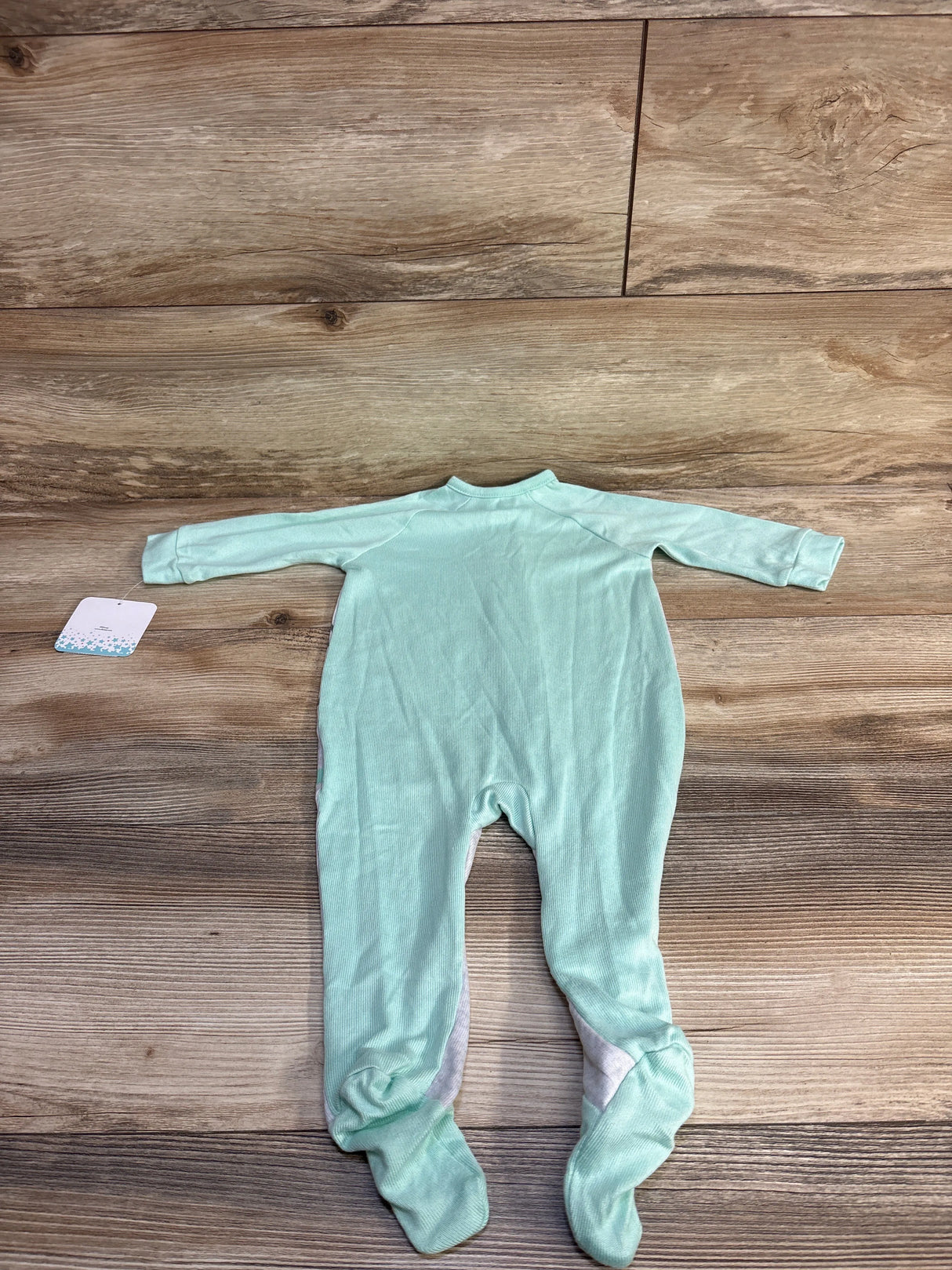 Back view of mint green Disney Dumbo footed sleeper showing long sleeves and attached size tag on wood floor