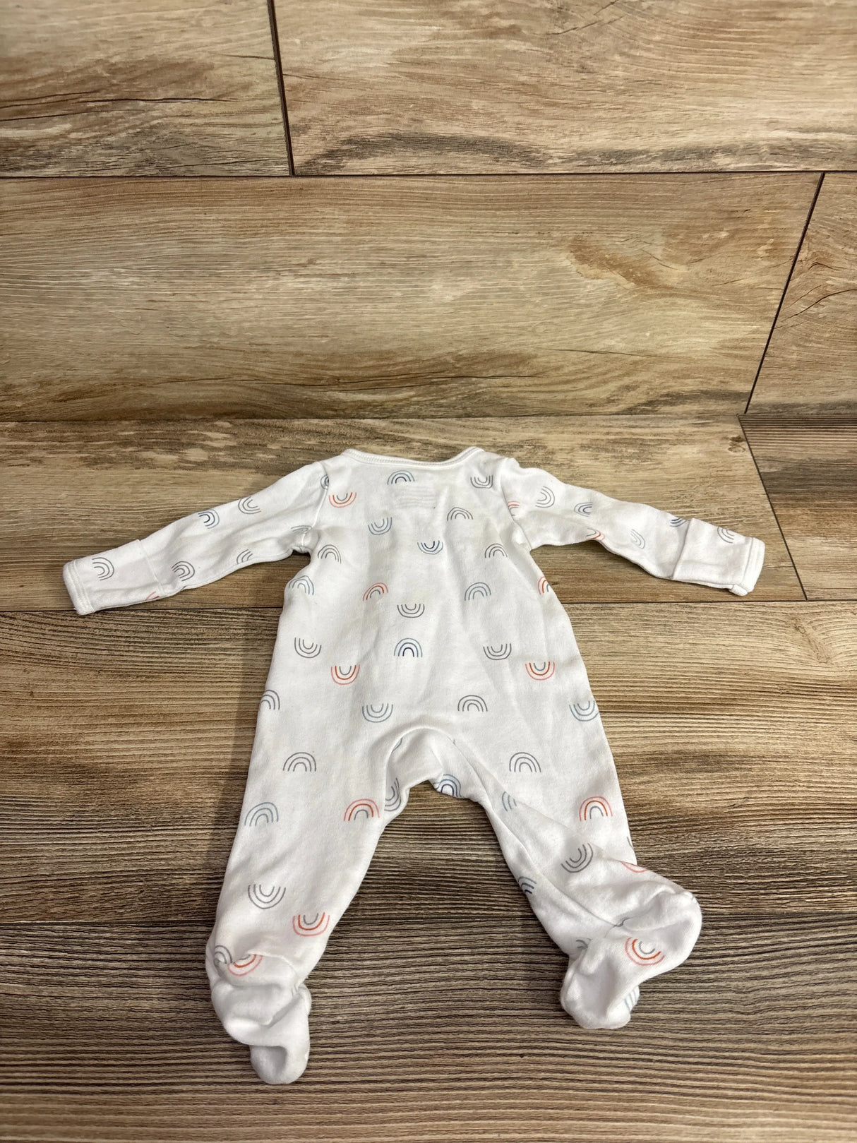 Flat lay of Simple Joys white preemie footed sleeper showcasing small multicolor rainbow print on wood floor background