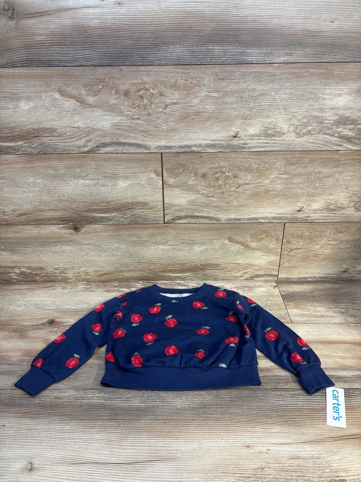 Navy blue kids sweater with red apple print, Carter's brand, laid on wood floor