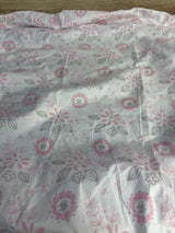 Top-down view of Peanutshell fitted crib sheet showcasing pink and gray floral pattern on white background with a folded edge and wood floor visible