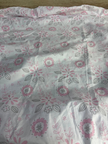 Top-down view of Peanutshell fitted crib sheet showcasing pink and gray floral pattern on white background with a folded edge and wood floor visible
