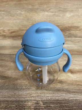 OXO blue handled sippy cup with straw on wood surface