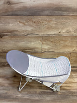 Side view of Summer Deluxe baby bather showing gray padded headrest and white mesh scallop pattern seat on wooden floor