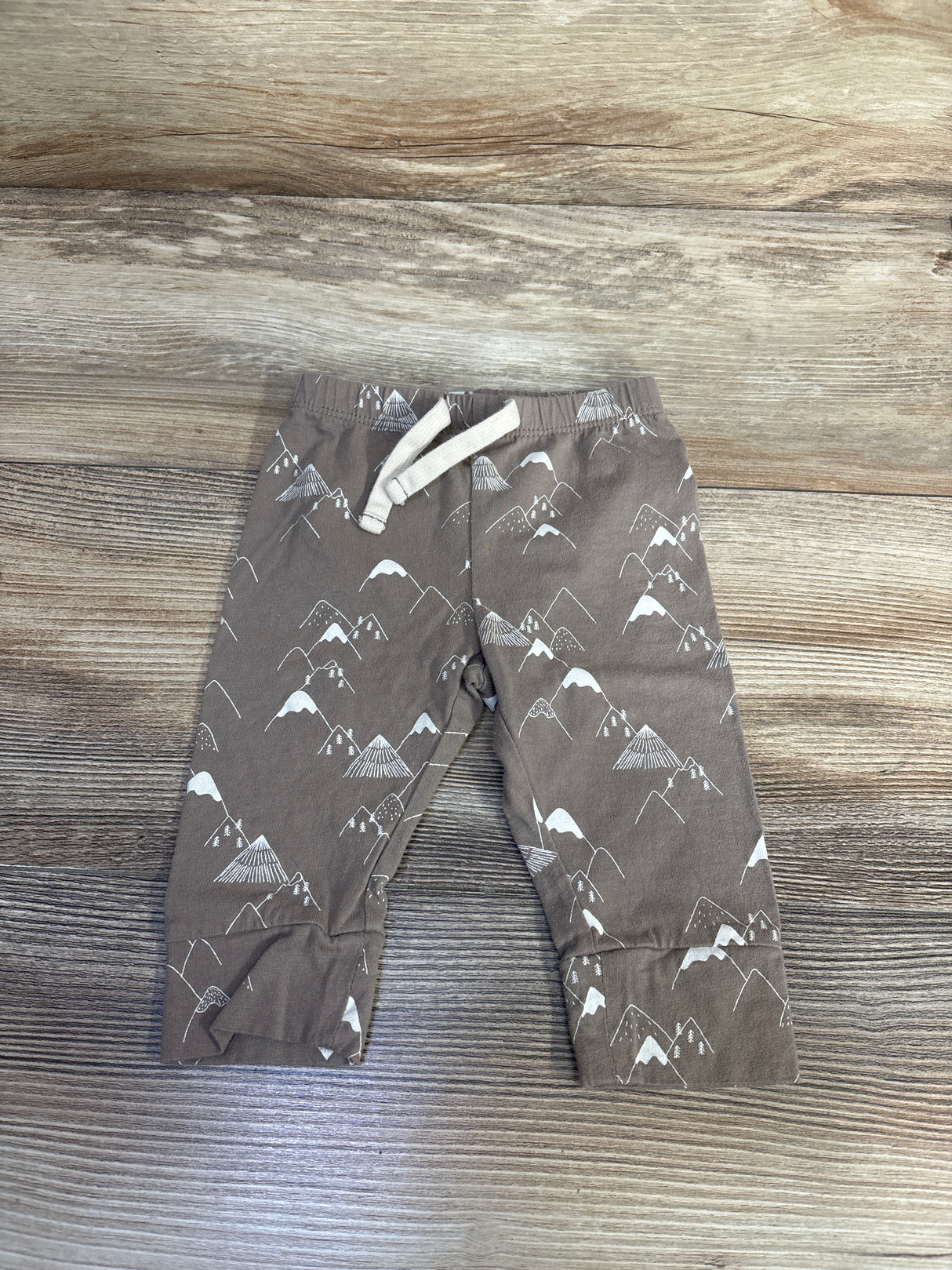 Top-down of Baby Gap brown mountain-print jogger pants (3-6 months) showing elastic waist with tie on wood background