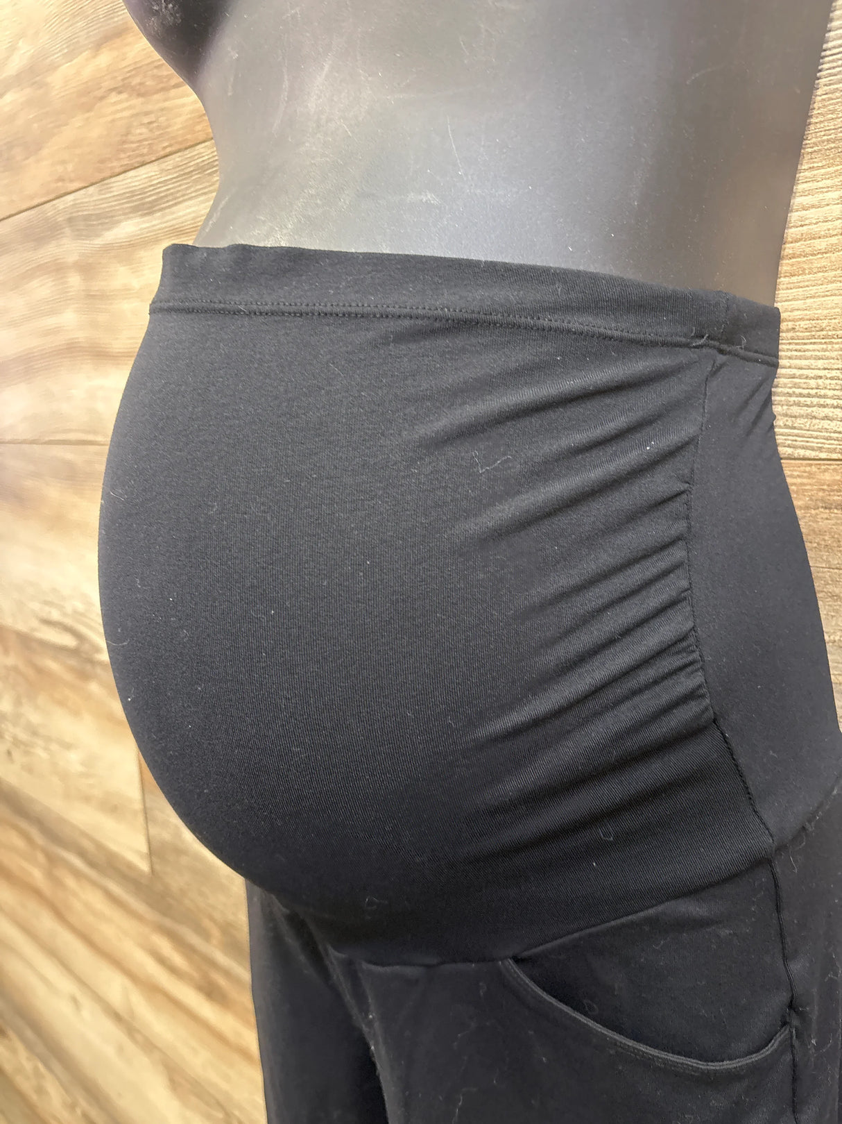 Side view of Ewedoos over-belly pants showing elastic belly panel and side ruching on mannequin with wooden wall