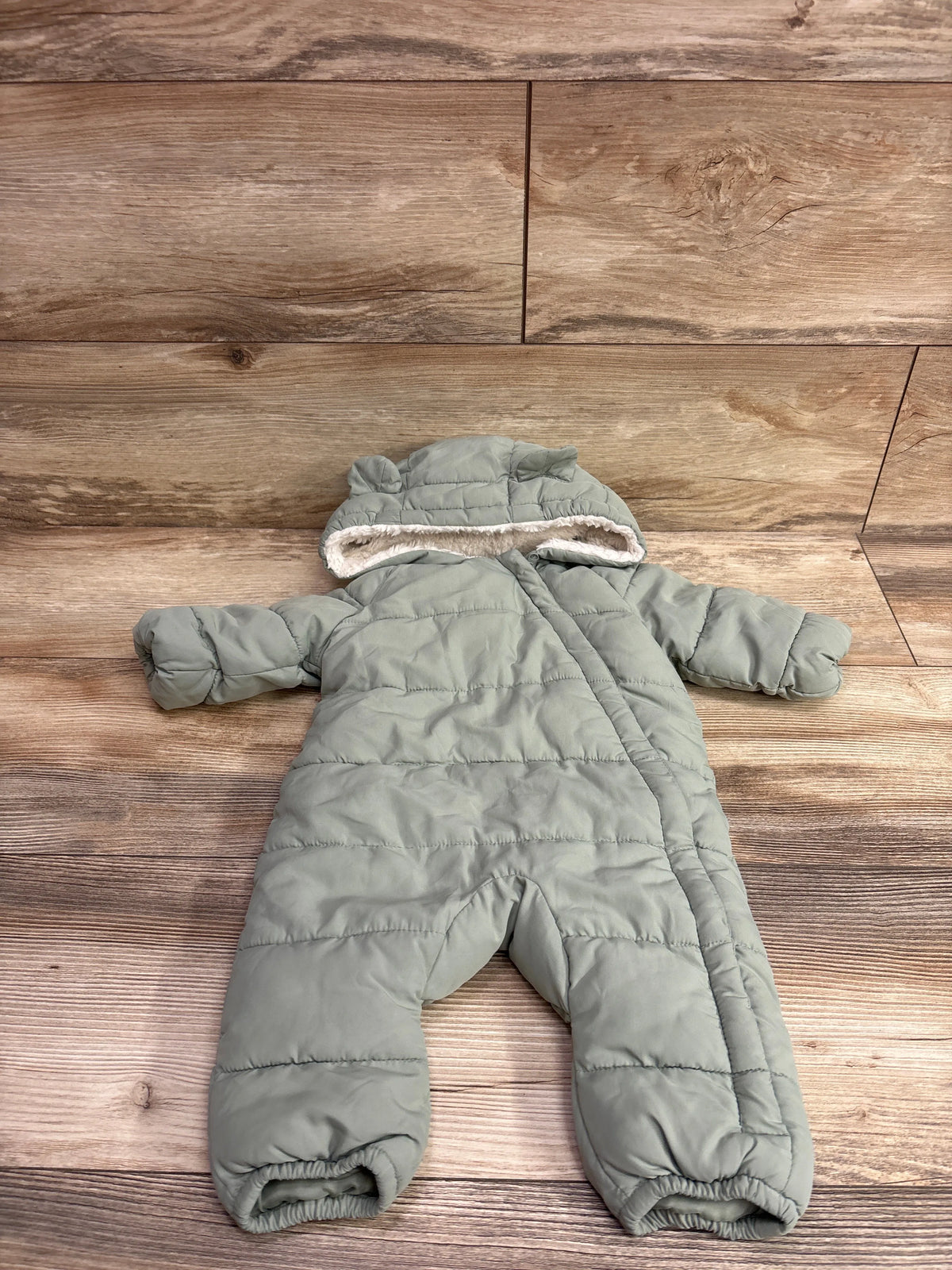 Top view of green fur-lined bunting for 1 to 3 months showcasing hood and quilted padding on a wood floor
