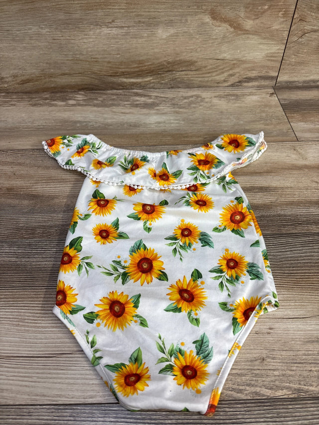 Flat lay of white off-shoulder baby romper showcasing sunflower print and ruffle trim, size 12 months, on wood floor