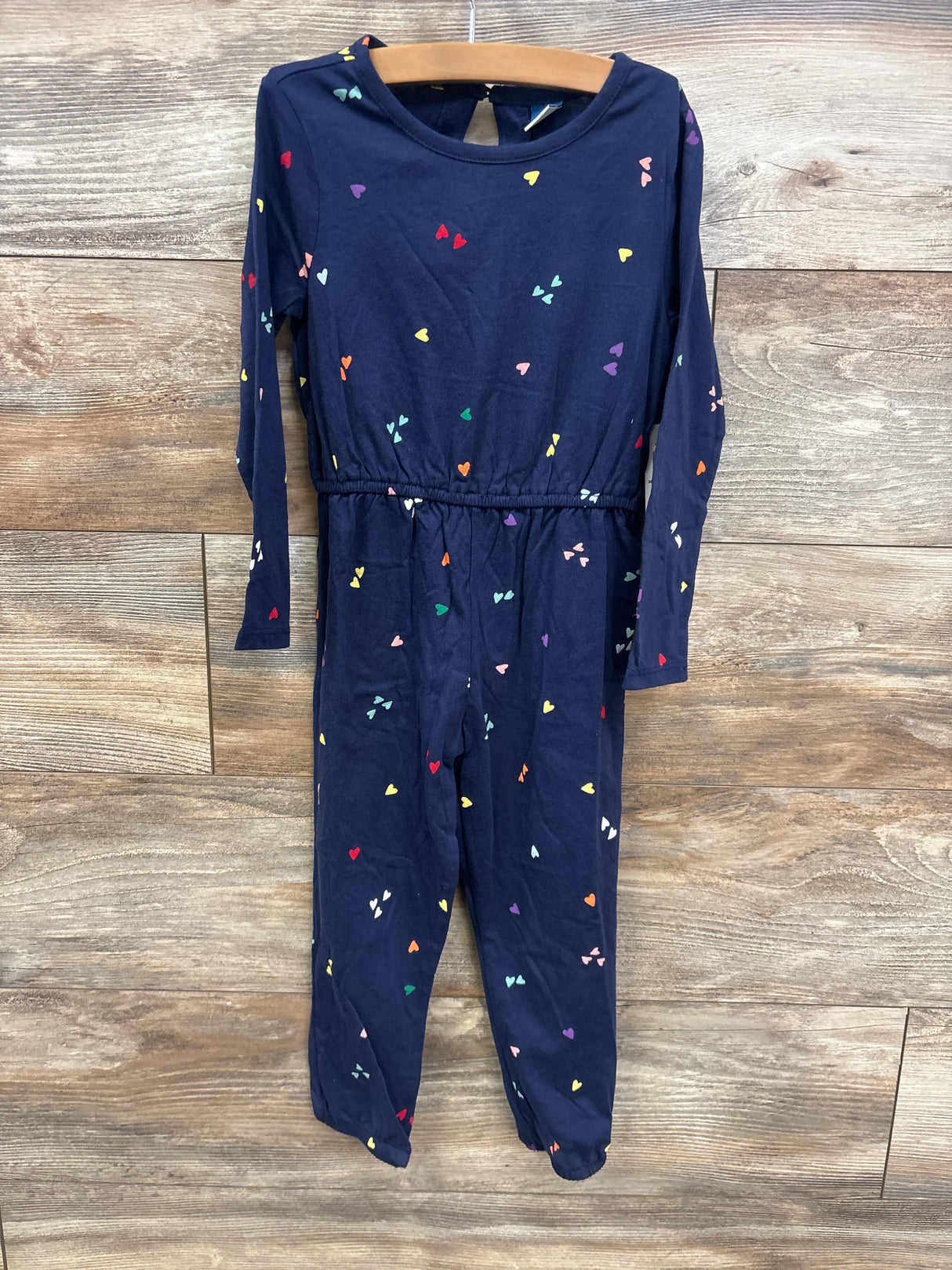 Navy blue toddler jumpsuit with colorful heart patterns hanging on wooden background