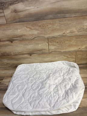 Top down view of Amfori waterproof crib mattress protector showing quilted top and elastic skirt on wood floor