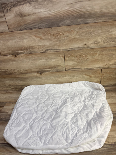 Top down view of Amfori waterproof crib mattress protector showing quilted top and elastic skirt on wood floor