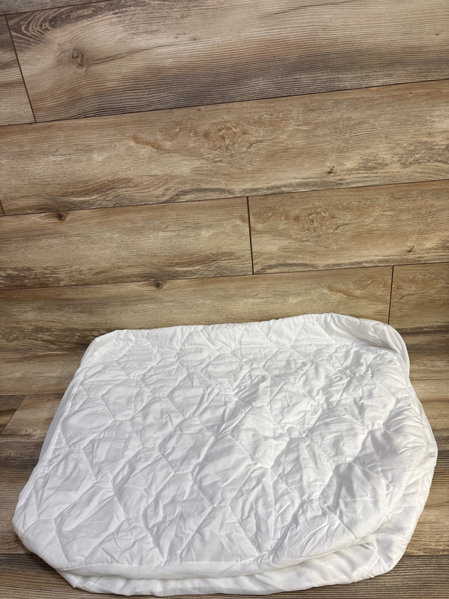 Top down view of Amfori waterproof crib mattress protector showing quilted top and elastic skirt on wood floor