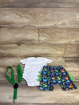 Flat lay of 3-piece baby dinosaur set: white onesie, navy dinosaur shorts with green spikes, green suspenders on wood
