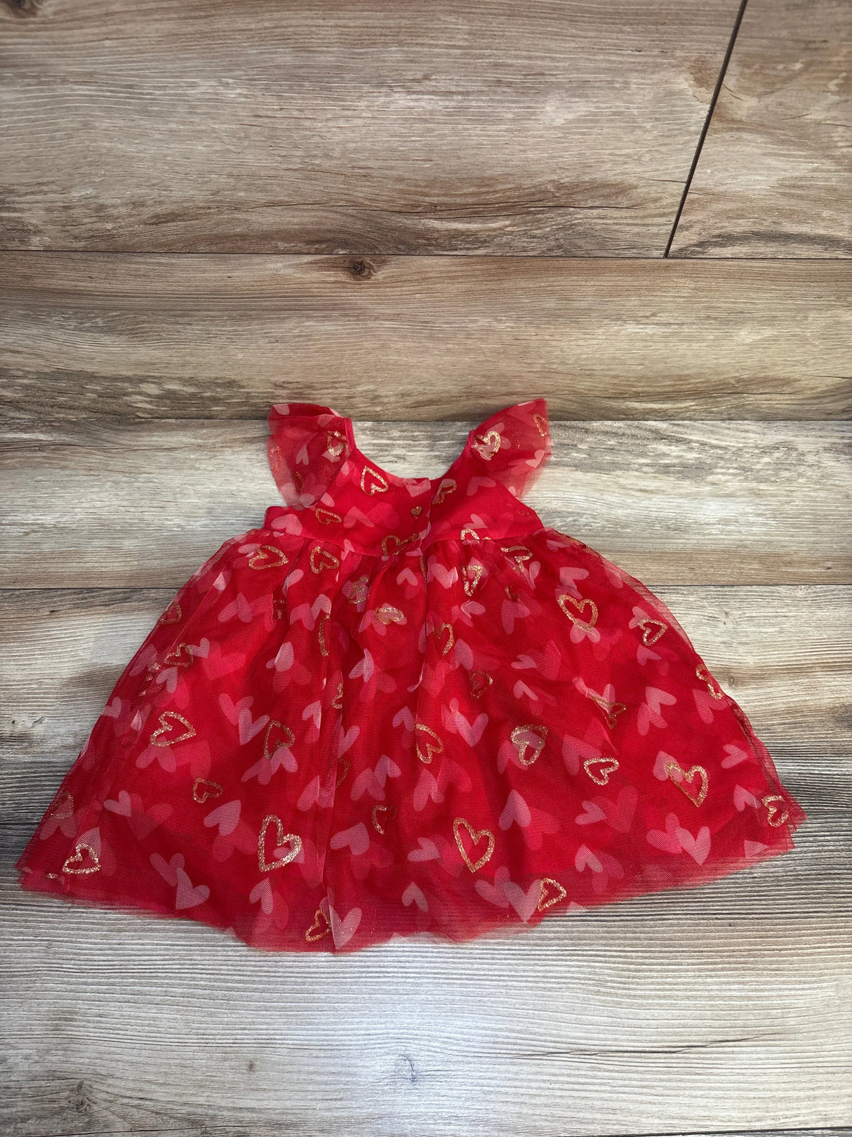 Red toddler dress with gold and pink heart prints, displayed on wood floor.