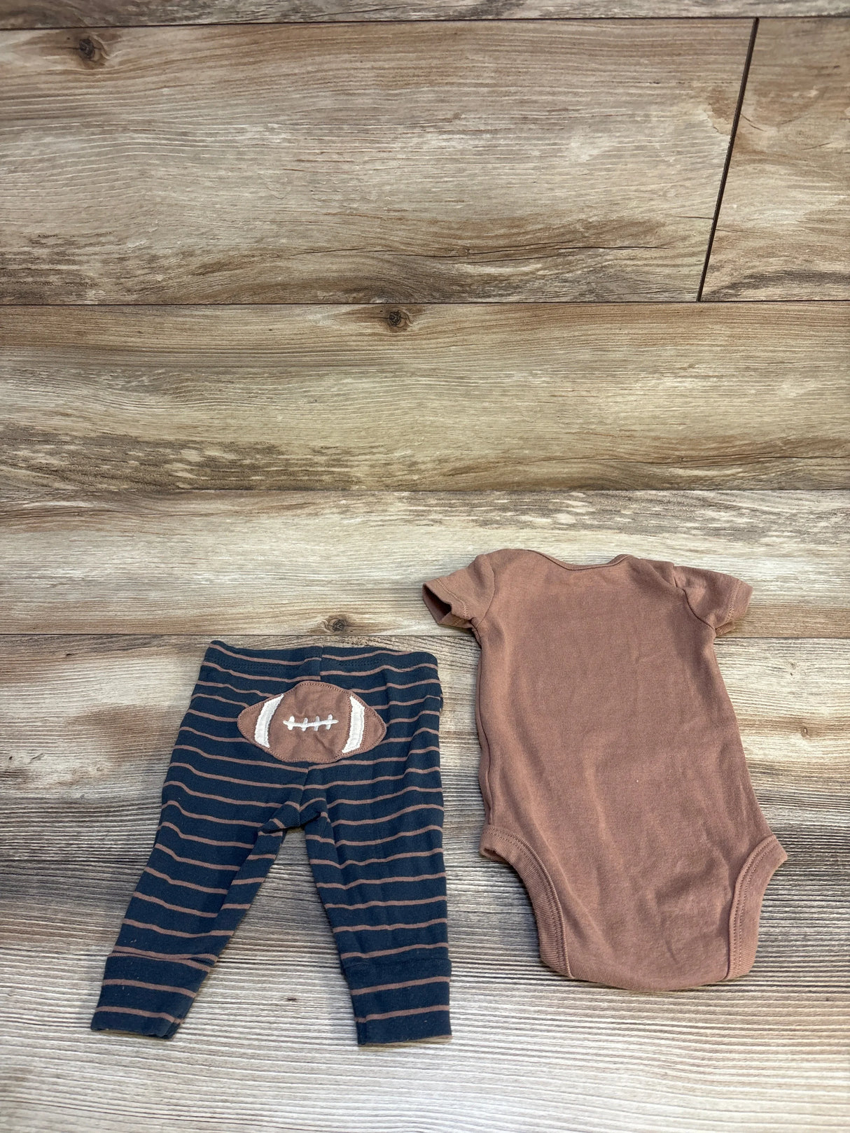 Brown baby bodysuit and striped football leggings on wood background
