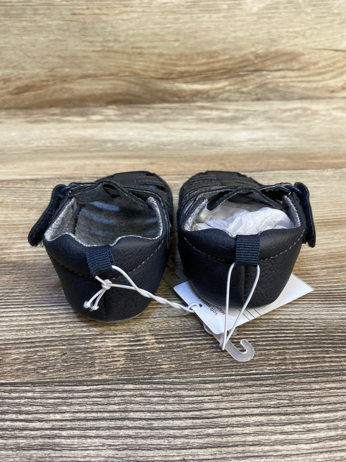 Back view of navy infant fisherman sandals showing heel loop, Velcro strap and attached size tag on wood background