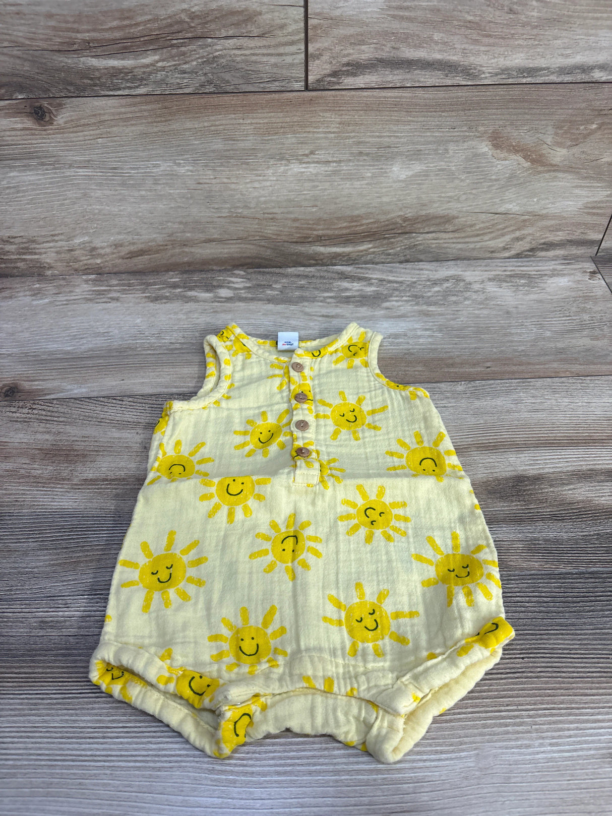 Flat lay of Old Navy sleeveless henley baby romper showing yellow smiling sun print and button placket on wood background