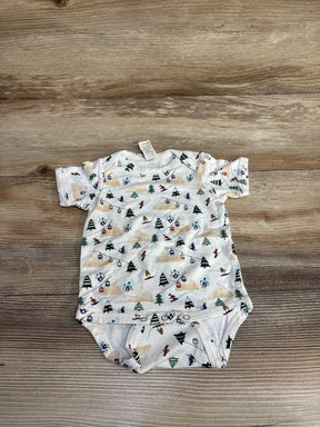 White baby onesie with ski-themed print of skiers, trees, and ski lifts on wooden background
