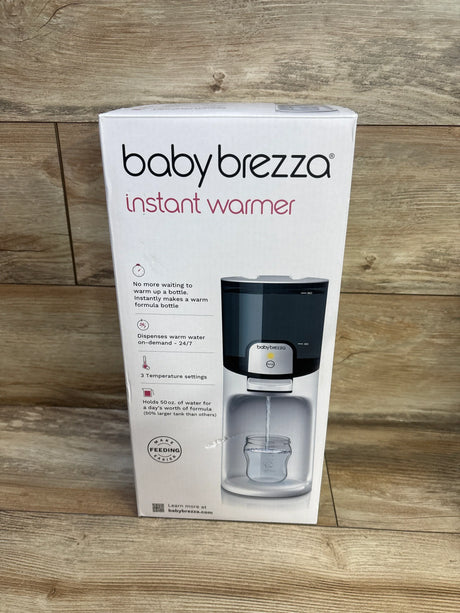 Front view of Baby Brezza Instant Warmer box showing the unit dispensing warm water into a baby bottle on wood floor