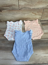 Top view of three Nicole Miller flutter-sleeve baby bodysuits (white floral, peach, blue) showcasing ruffled sleeves on wood background