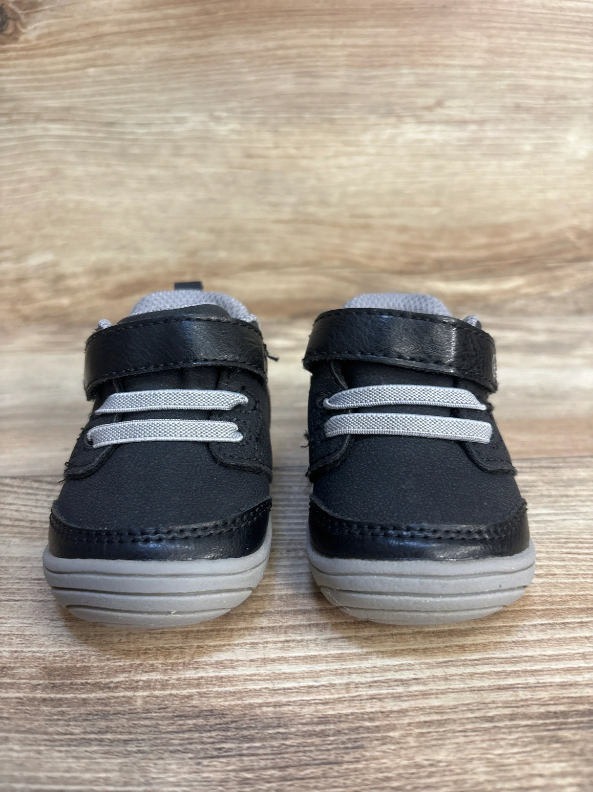Black and gray toddler sneakers with velcro straps on wooden background