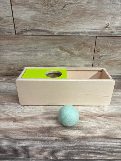 Front view of Lovevery Sliding Top Box showcasing a green sliding top and blue ball with a wood floor background
