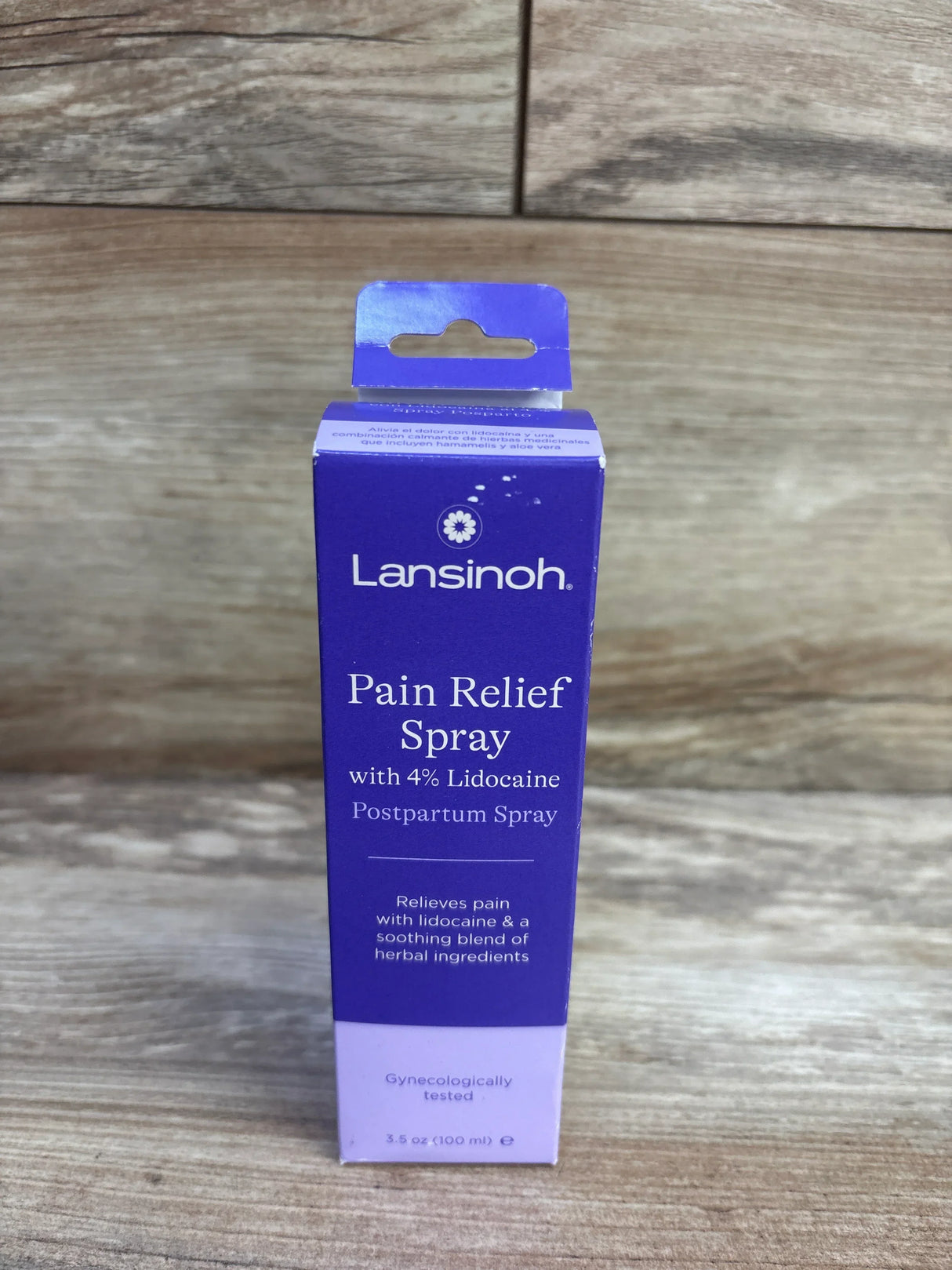 Front of Lansinoh postpartum pain relief spray box showing '4 percent lidocaine', 3.5 oz, purple box on wooden tabletop