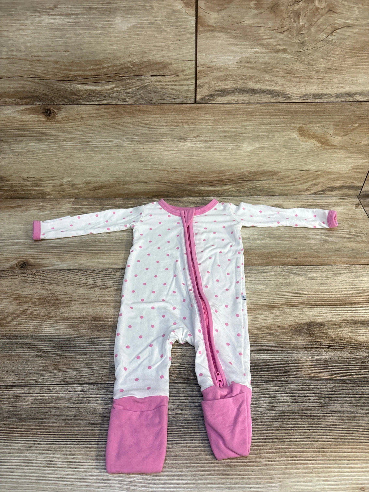Pink polka dot baby onesie with zipper, laid flat on wood floor