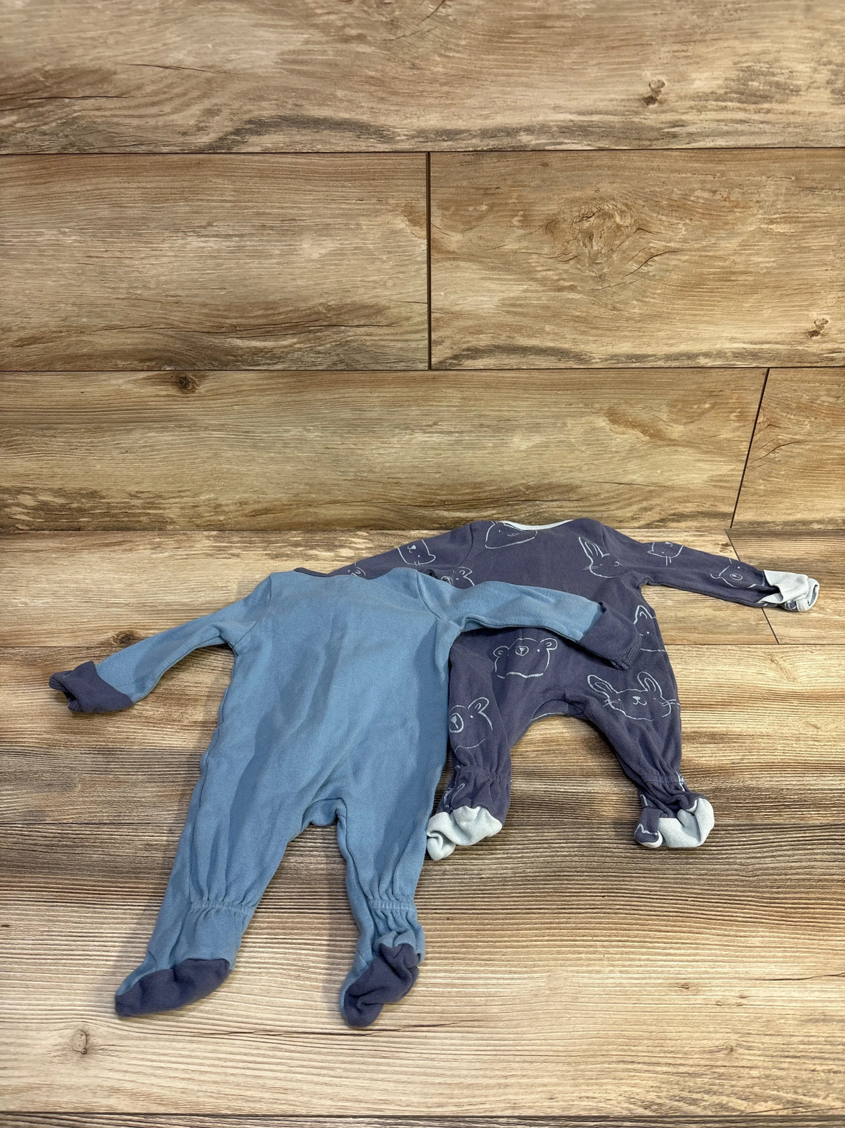 Top view of two Cloud Island footed newborn sleepers, solid light blue and navy animal print on wood