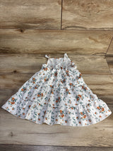 Front view of white tiered baby dress, orange floral print, thin straps and ruffled tiers on wood background
