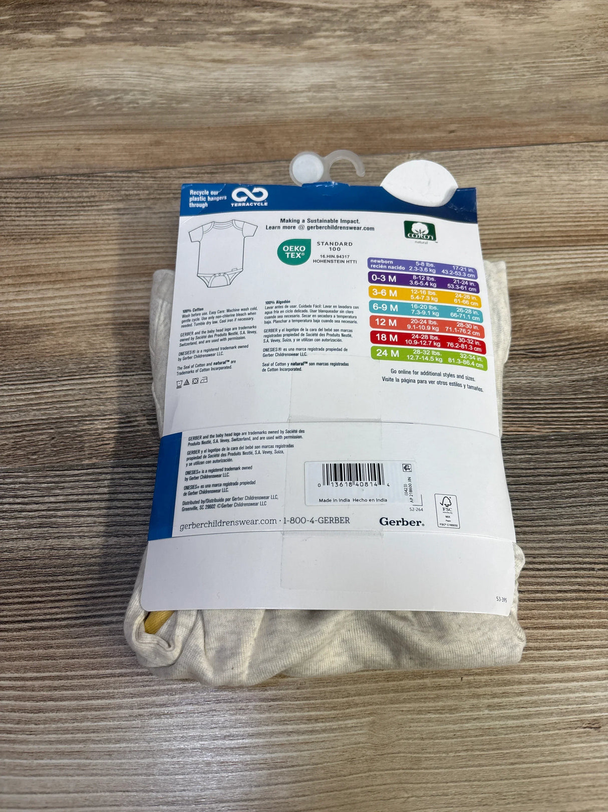 Back view of 3-pack Gerber beige baby bodysuits showing packaging label with size 6-9 months on wood tabletop