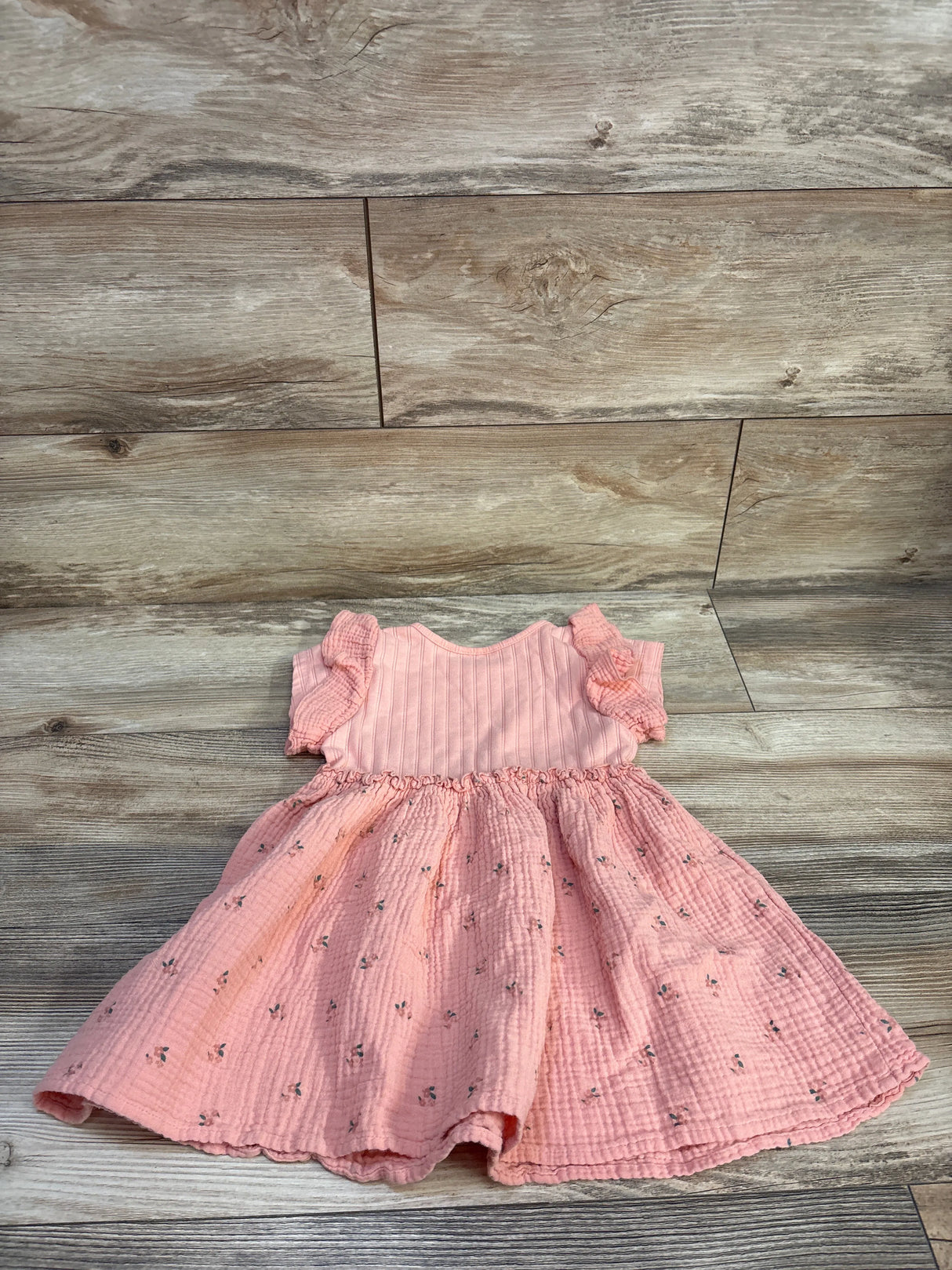 Flat lay of pink Disney Junior Minnie Mouse muslin toddler dress showing ruffled short sleeves and gathered floral skirt on wood background