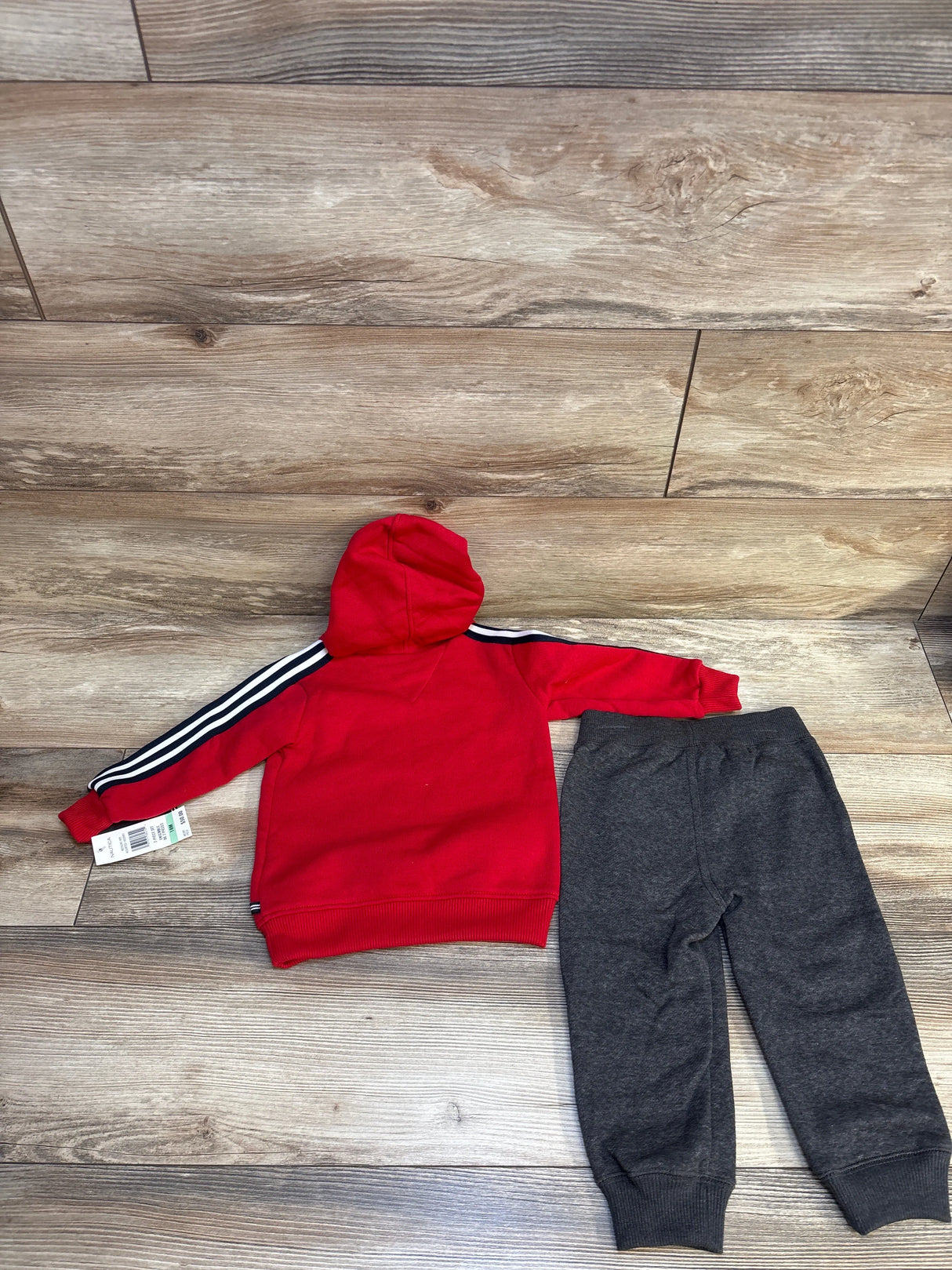 Red hooded sweatshirt with striped sleeves and gray jogger pants set for kids, laid on wood floor