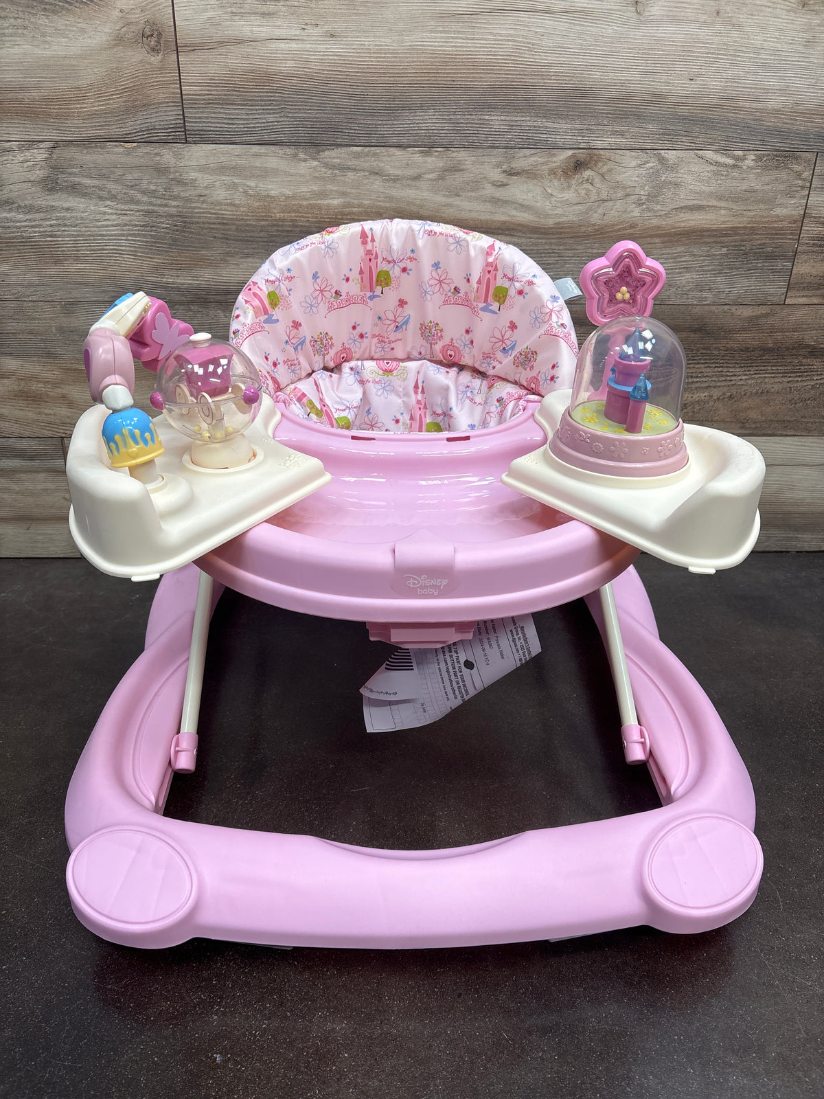 Front view of Disney Music & Lights Baby Walker in Happily Ever After showcasing pink padded floral seat and activity toys with a wood backdrop