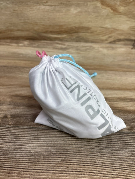 Angled view of white Alpine Muffy Baby ear muffs pouch showcasing pink and blue drawstrings on a wood-grain surface