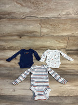 Three baby boy long-sleeve onesies with stripes, mountain, and dinosaur prints on wood floor