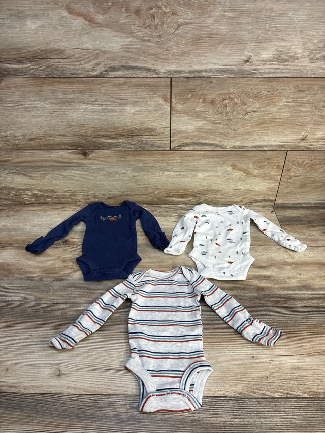 Three baby boy long-sleeve onesies with stripes, mountain, and dinosaur prints on wood floor