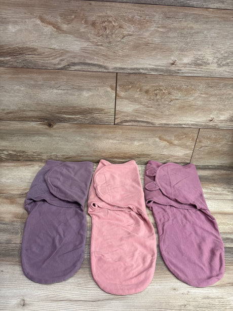 Three Comfy Cubs swaddle wraps in purple, light pink, and mauve on a wooden surface.