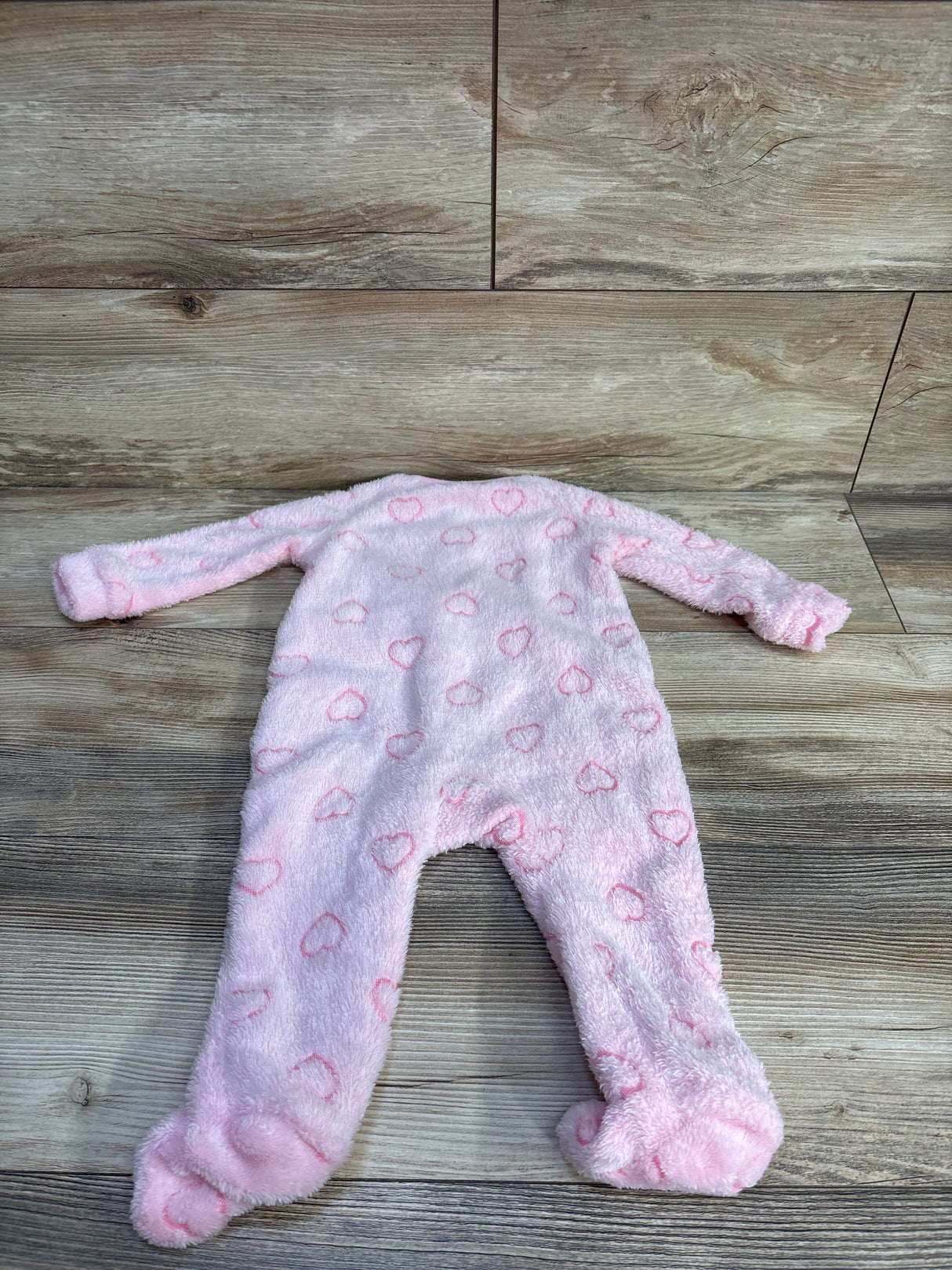 Front flat lay of plush pink blanket sleeper showcasing raised heart pattern and built-in footies on wood plank background