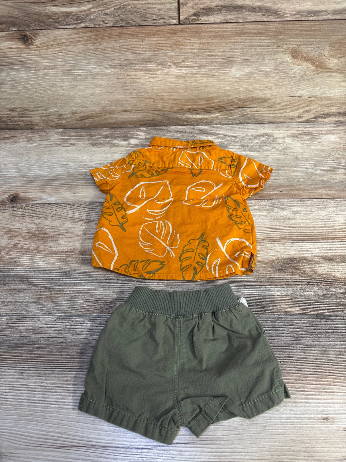 Flat lay of Carter's newborn 2-piece set: orange leaf-print button-up shirt and olive elastic-waist shorts on wood background