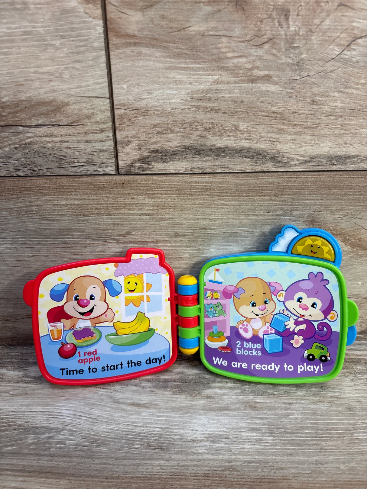 Open Fisher-Price Counting with Puppy electronic toy book showing two illustrated pages with breakfast and play scenes on a wood floor